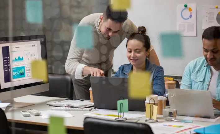 A group of professionals collaborates around a table with laptops, charts, and sticky notes, discussing data insights and strategies